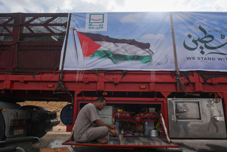 A man sits near a truck carrying humanitarian aid to Palestinians, on a desert road (Cairo - Ismailia) on the way to the Rafah border crossing to enter Gaza