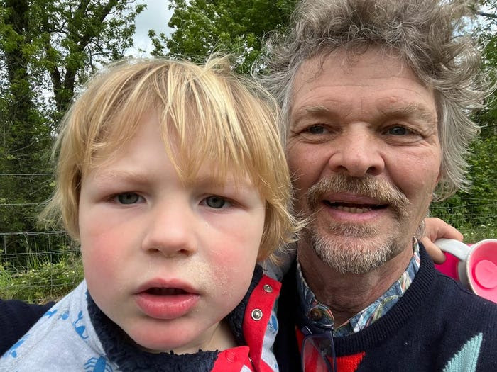 Barnaby Browsell, who looks more like a four-year-old than a two-year-old, is carried by his father, Peter, in a park with trees.