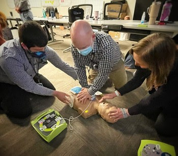 Photo of three people using an automated external defibrillator on a human dummy