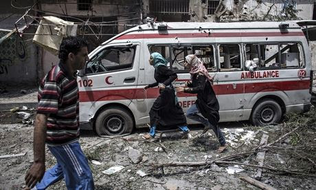Two Palestinian girls run past a damaged ambulance in Gaza