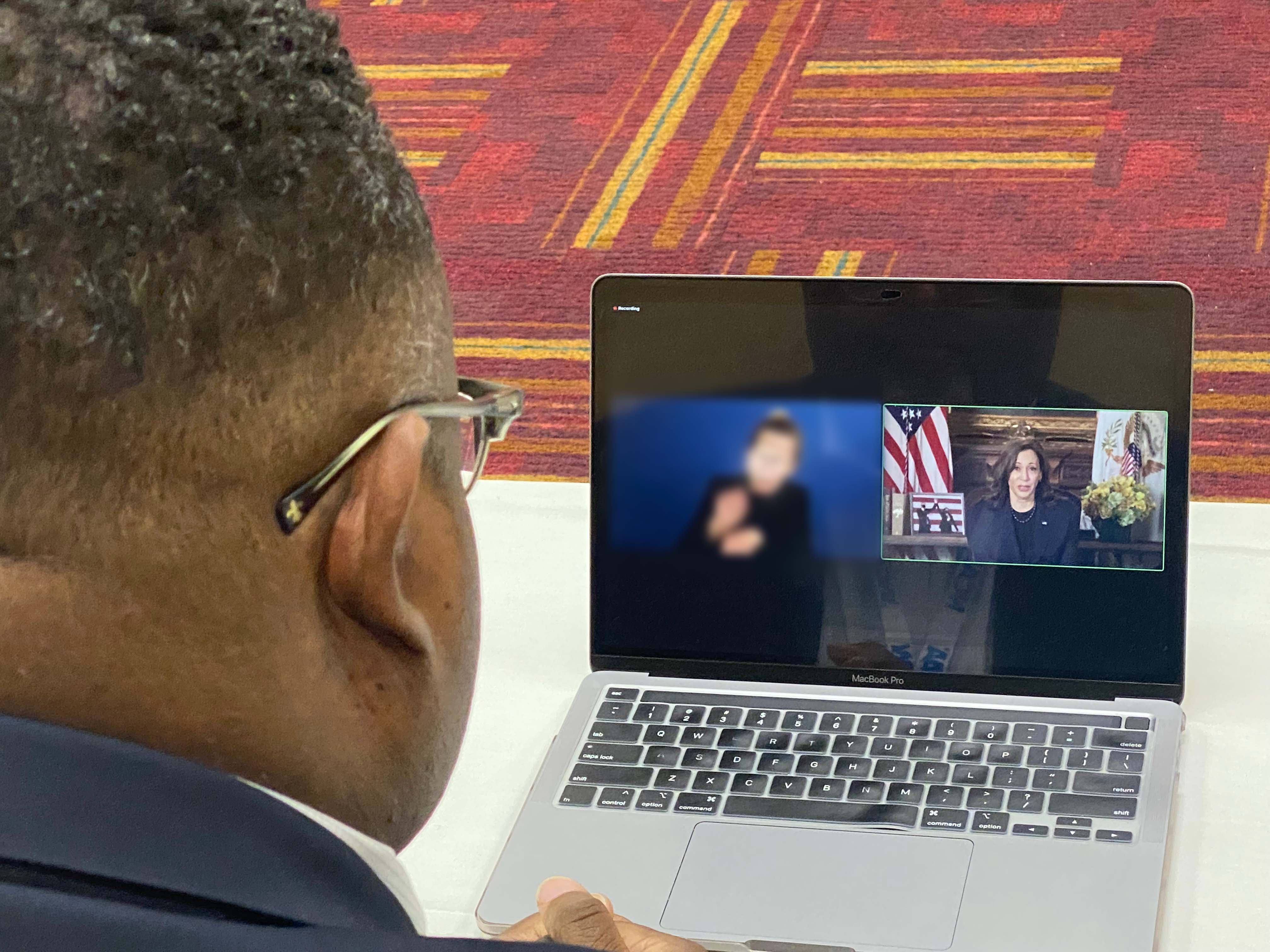 Kean President Repollet at a desk viewing a President Harris speak in a virtual meeting.