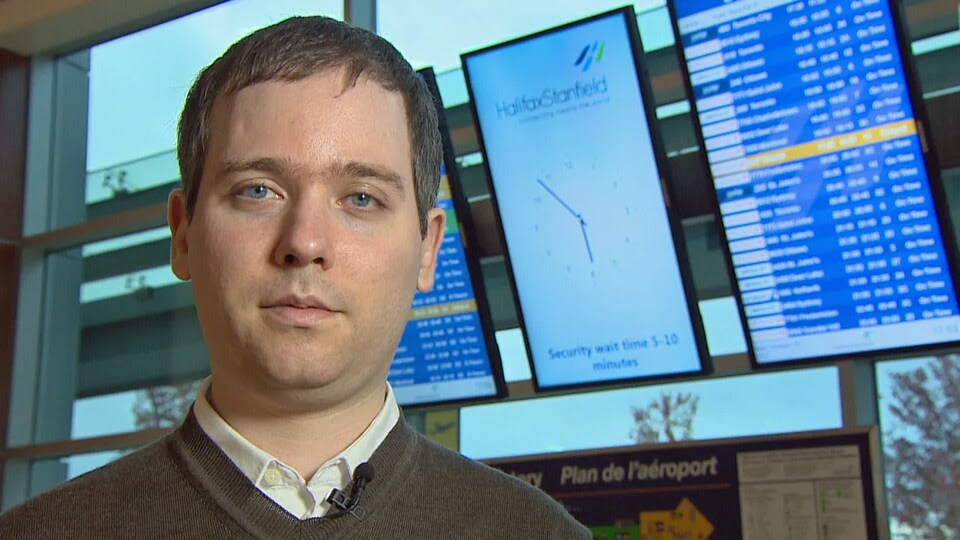 Gabor Lukacs se tient debout devant un panneau d'affichage de vols d'avions dans un aéroport.