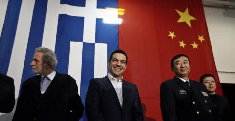 El primer ministro griego Alexis Tsipras sonríe delante de una bandera griega y una china, antes de su discurso en el buque 'Changbaishan', en el ateniense puerto de El Pireo. REUTERS / Alkis Konstantinidis
