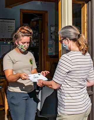 A masked, female DNR parks and recreation seasonal worker helps a woman with camping check-in