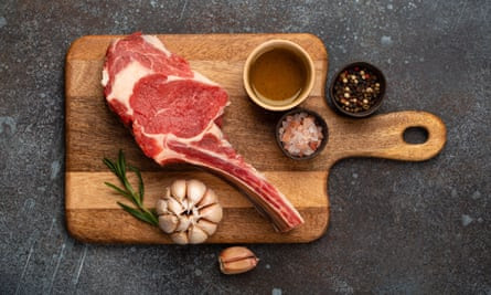 A cut of raw beef on a wooden board with garlic clove, salt and sauce.