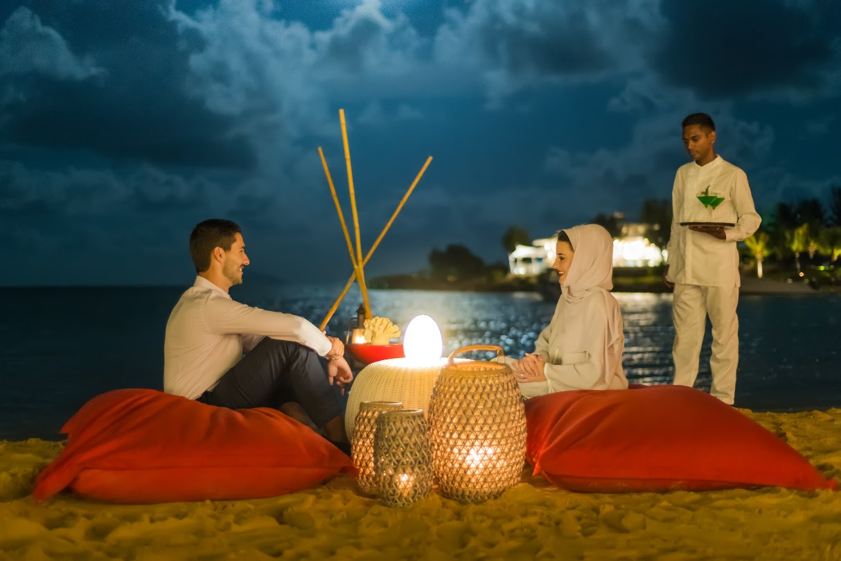 A group of people sitting on a beach with a fire pit and candlesDescription automatically generated
