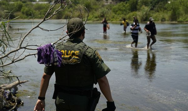 In this June 15, 2021, file photo a Border Patrol agent watches as a group of migrants walk across the Rio Grande on their way to turn themselves in upon crossing the U.S.-Mexico border in Del Rio, Texas. (AP Photo/Eric Gay, File)