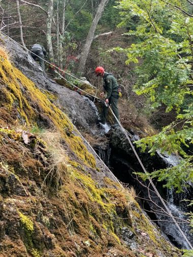 Ranger uses ropes on the side of a steep cliff in the woods during training