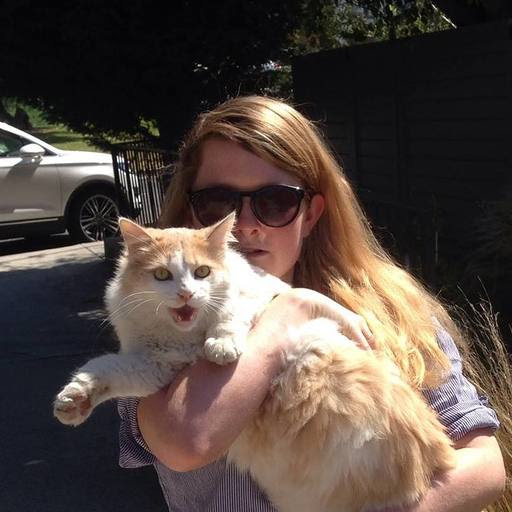 A woman with long hair holds a white and ginger cat in her arms.