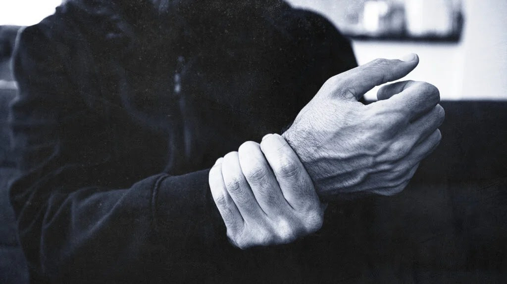 A black-and-white image of an older adult holding their wrist due to joint pain caused by hepatitis C.