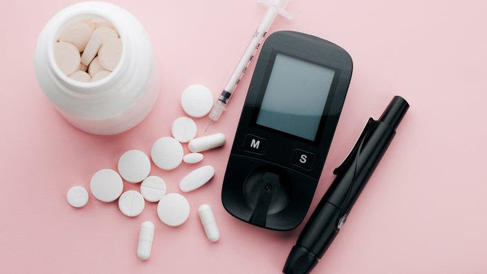 Supplements and diabetes supplies on a pink background.