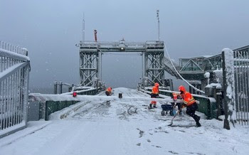 Four people shoveling snow and/or treating the surface with salt on the vehicle transfer span at a ferry terminal