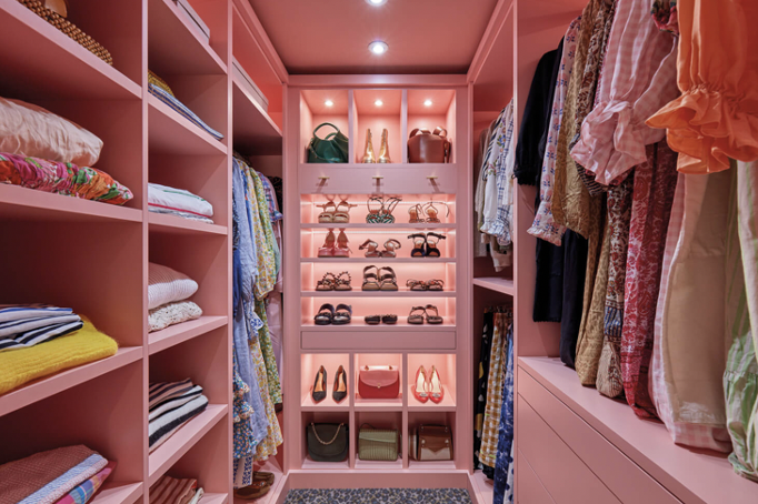 a pink wooden bespoke walk-in wardrobe from Neville Johnson containing lots of pairs of shoes, bags and dresses