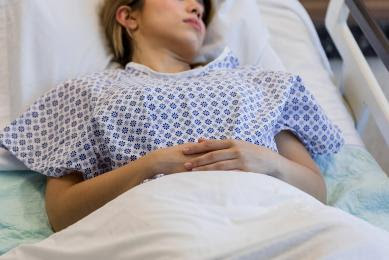 The female patient lays down in the hospital bed with her hands crossed while she tries to rest.