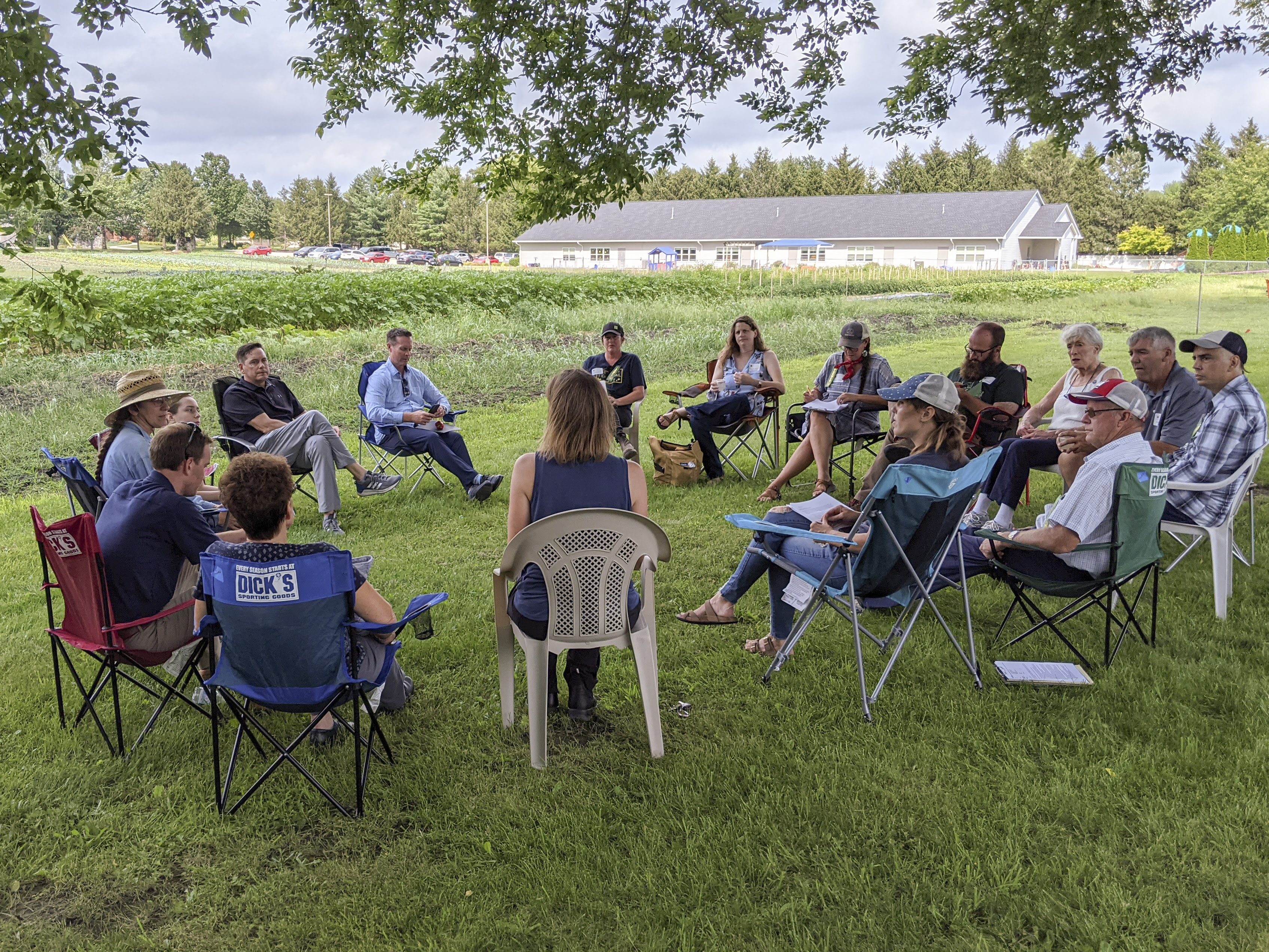Over twenty farmer roundtable participants are seated in a circle over looking the large fields of food being grown at Sola Gratia. 