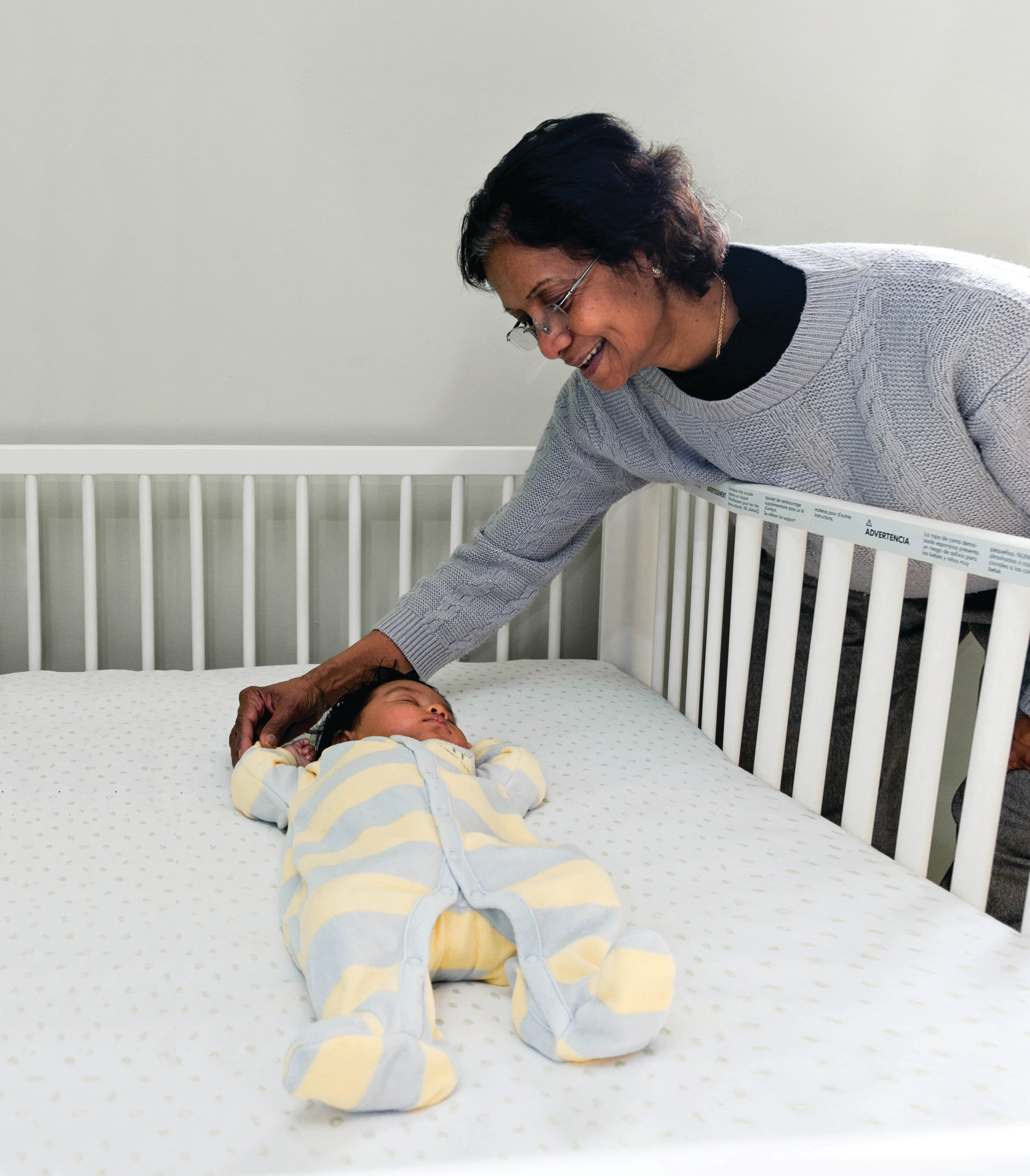 Grandmother looking at her grandson sleeping in a crib