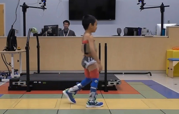 A child walking with the assistance of a wearable robotic device called an exoskeleton.