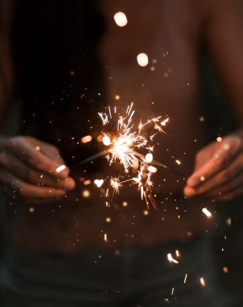 A person holds a flickering sparkler between their hands; it illuminates a small area with its glow