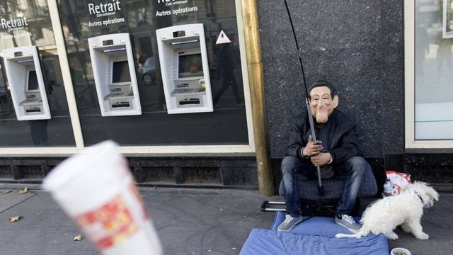 Um homem pedindo dinheiro em frente a caixas eletrônicos