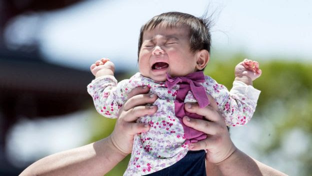 Bebê japonês chora enquanto é erguido por uma pessoa