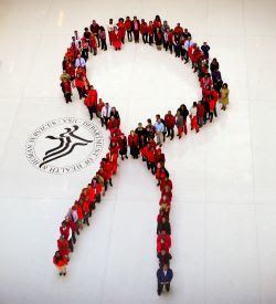 a human hiv/aids ribbon - an image from high above of about 100 people wearing red and standing in the shape of the red hiv/aids ribbon