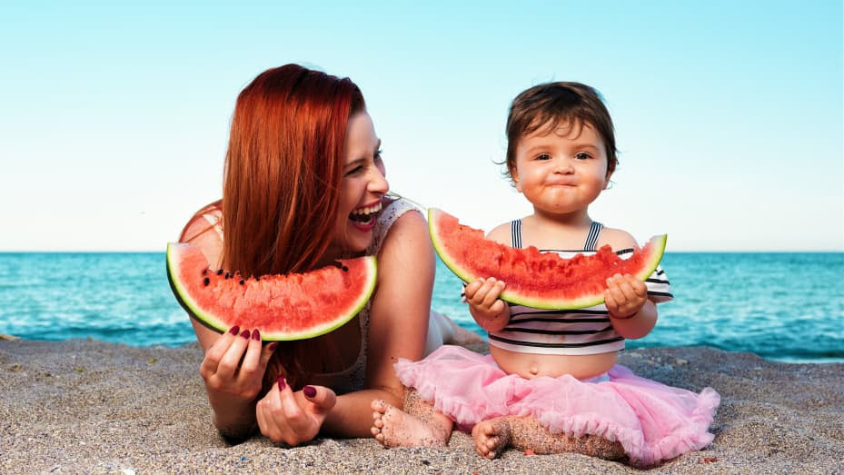 mom and daughter eating watermelon on a beach