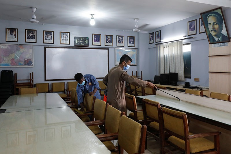 Employees spray sanitizer and clean chairs in the library at a school in Karachi, Pakistan