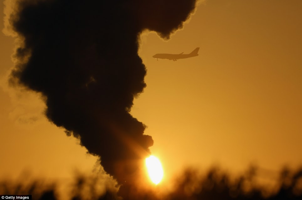 An aircaft can be seen against the mustard-yellow sky as cold weather accentuates the steam from a grass dryer in the Cheshire countryside 