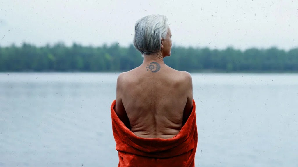 person with short white hair facing away with their back uncovered and a tattoo of a moon and sun on their back