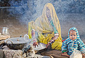 (c) 2014 Louis Kleynhans, Courtesy of Photoshare. Woman seated next to smoking stone cookstove, young child seated next to her.