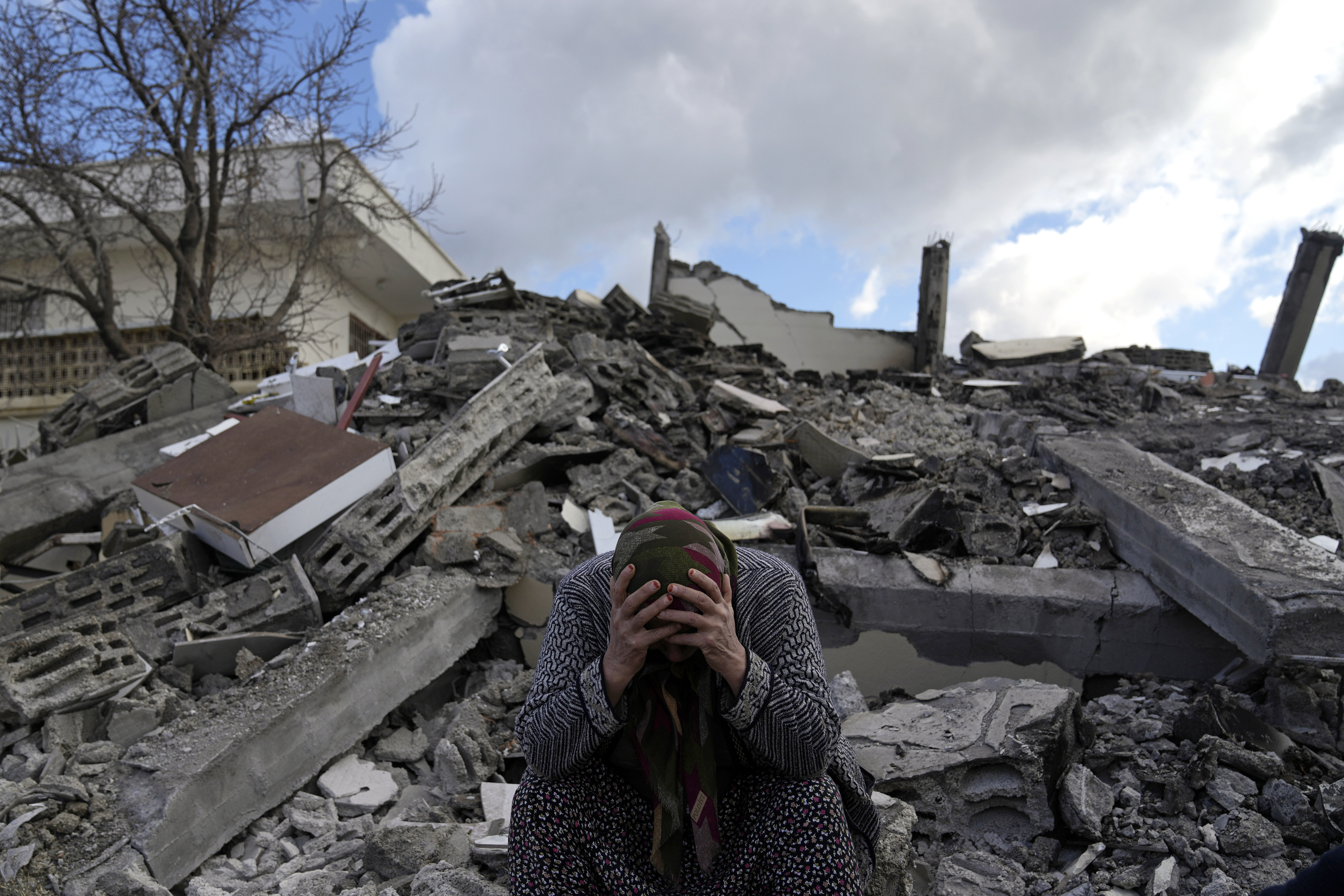 A woman sits on the rubble as emergency rescue teams search for people under the remains of destroyed buildings in Nurdagi town on the outskirts of Osmaniye city southern Turkey
