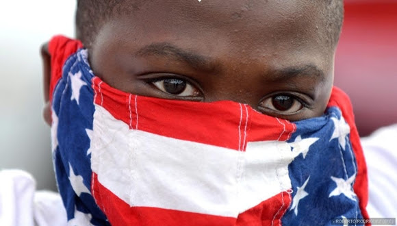 Un joven se tapa la cara con una bandera estadounidense durante la marcha de este lunes.