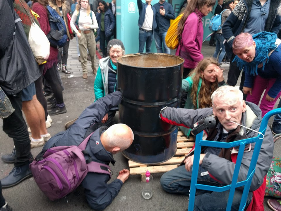 4 rebels blocking a road with an arm each locked into a black oil barrel.