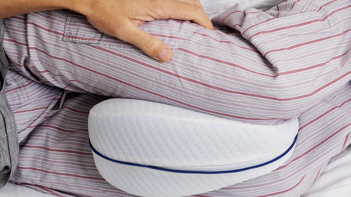 Close-up shot of a man sleeping with a pillow in between his knees.