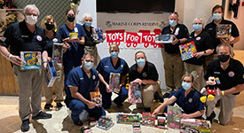 NDMS team holding donated toys in front of Toys for Tots sign