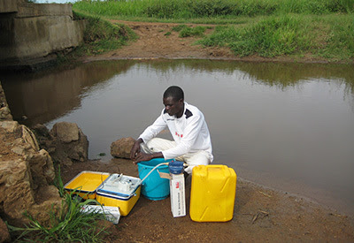 disease detective gathers a water sample in Uganda to test for water safety