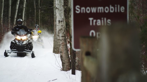 snowmobile on snowytrail with sign in foreground that reads "snowmobile trails open"