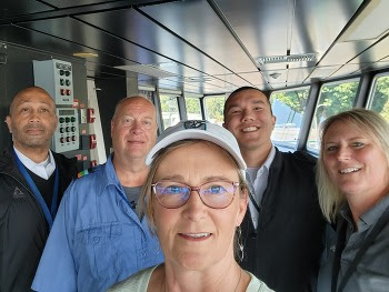 Five people pose for a selfie in the pilothouse of a ferry