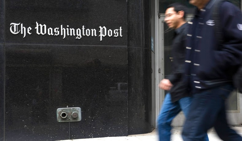 Two people walk briskly in front of The Washington Post building 