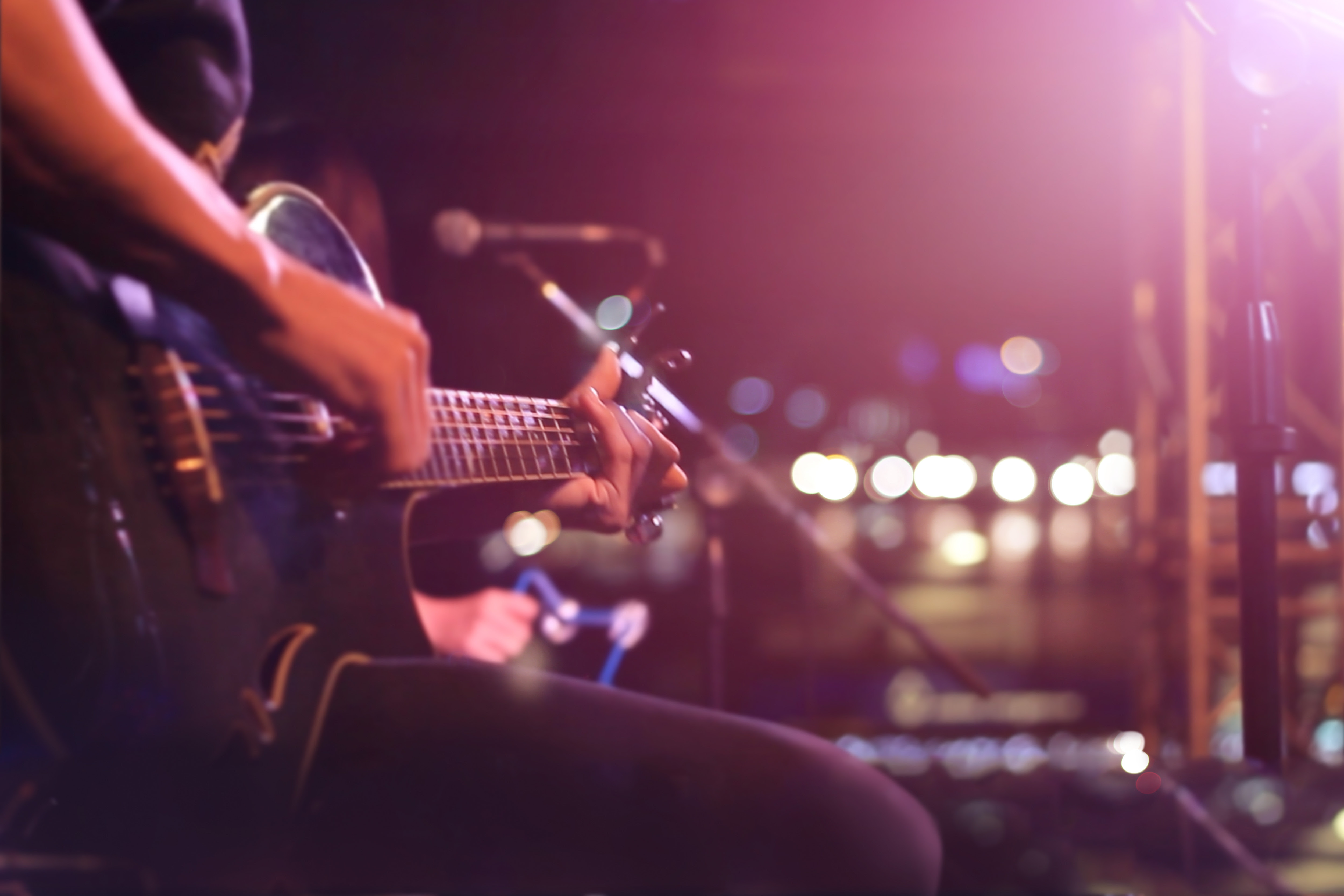 Person playing guitar with bright stage lights behind