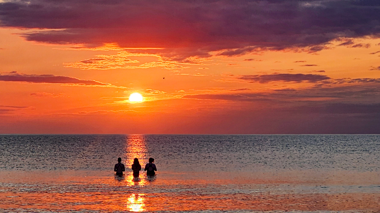 Three people in the water at sunrise.