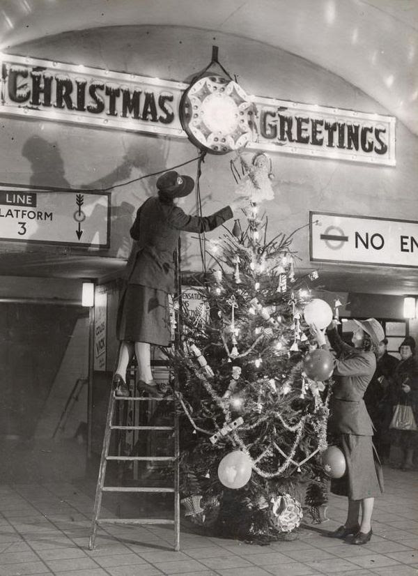 Black and white photo of people decorating a Christmas tree inside a station