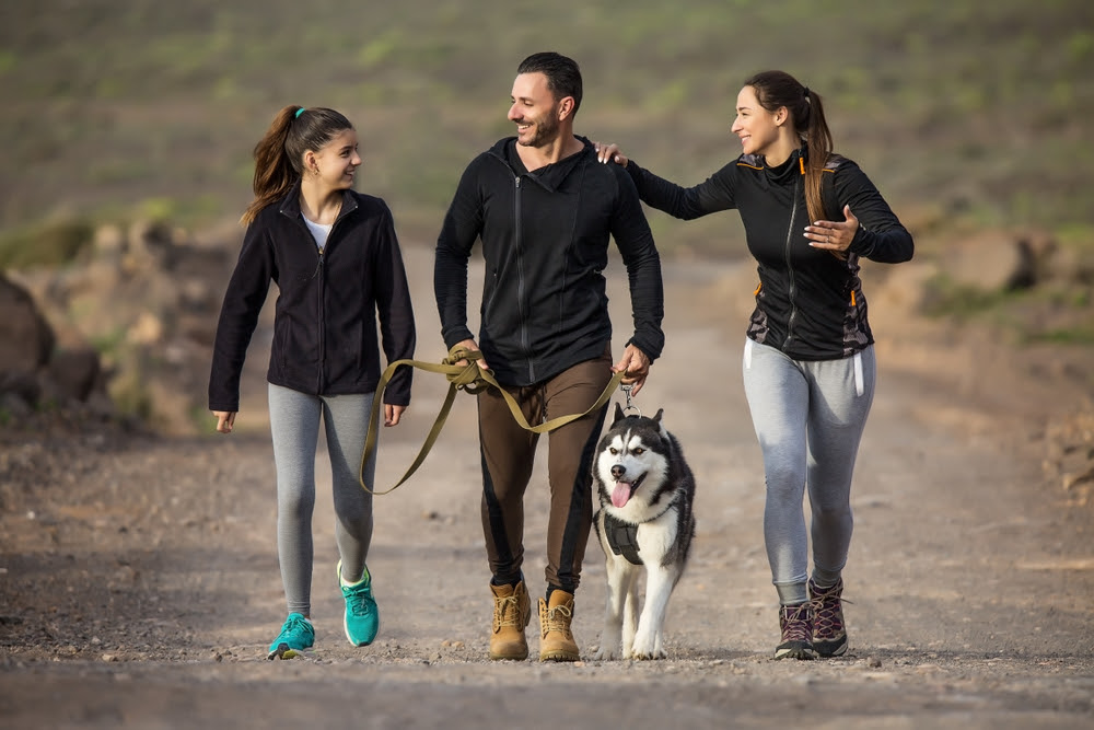 man and woman walking a dog with their teenage daughter