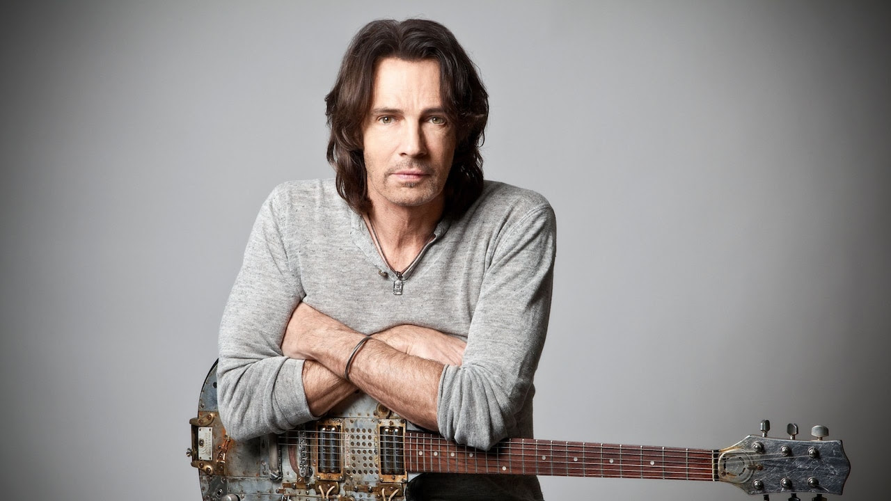 Artist Rick Springfield sits with his guitar resting on his lap