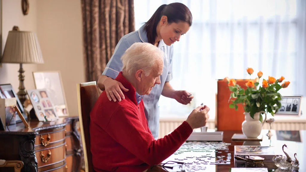 A caregiver helps a senior man with a puzzle, and although Medicare can medicare sometimes pay for a caregiver, this is out-of-pocket.