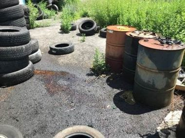 Photo of oil drums and old tires, some of the oil drums leaking onto the pavement
