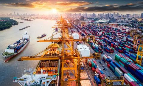 A busy port in Thailand with a city in the background, ships on the water and lots of shipping containers in port.