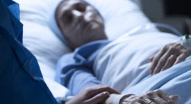 caregiver holding the hand of a hospice patient in a bed