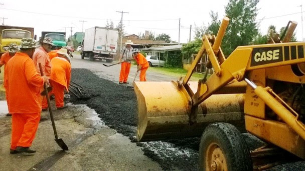 A foto mostra uma equipe de operários do Daer em obras na ERS-786, em Quintão. O grupo usa um trator e pás para aplicar asfalto na rodovia.