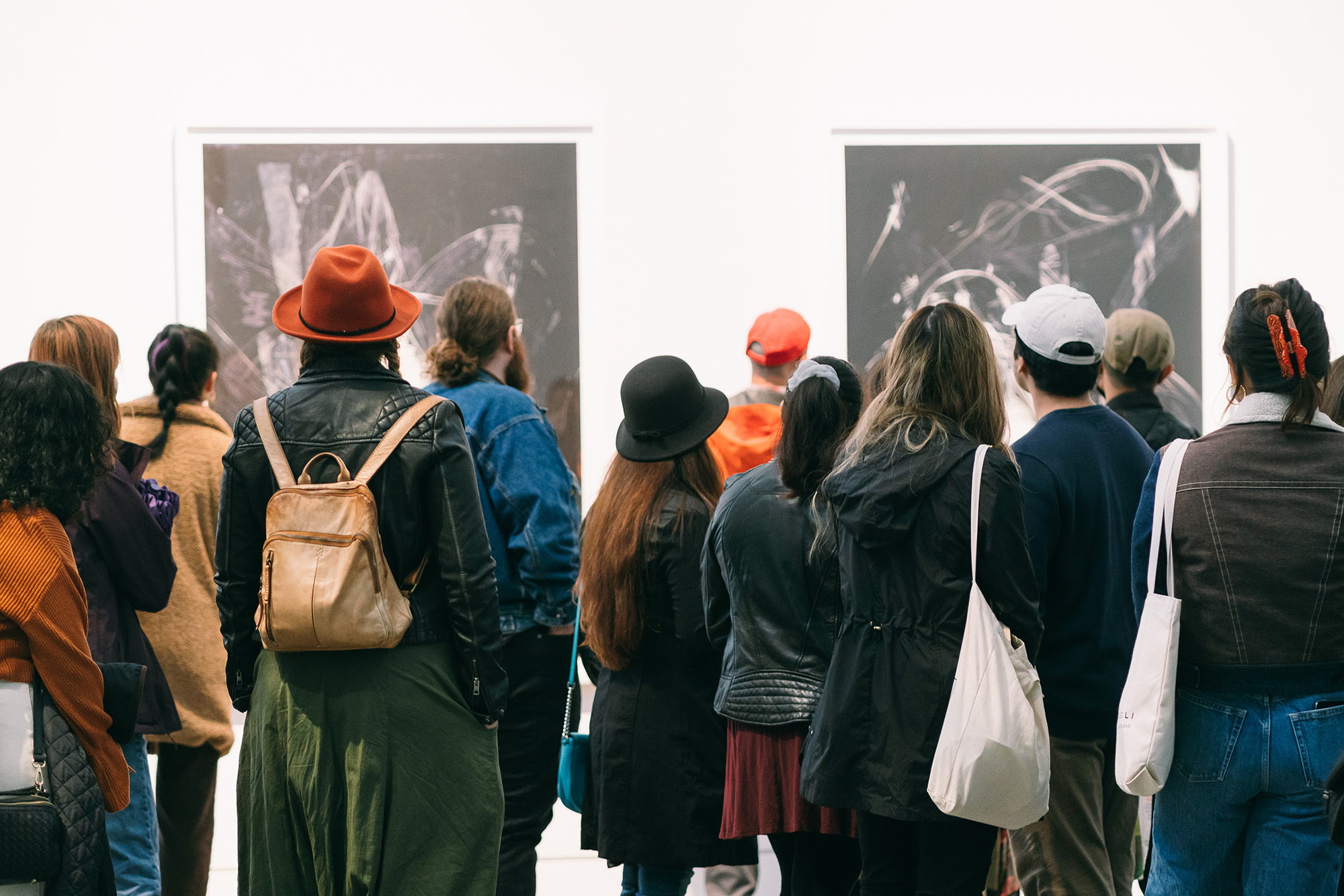A group of a dozen of visitors seen from the back looking at two large prints by artist Charisse Pearlina Weston.